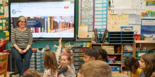 An educator smiles in front of a classroom full of engaged students