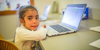 Little girl wears headphones and sits at a laptop