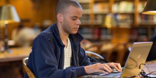 A patron types on a laptop inside of the Rose Main Reading Room
