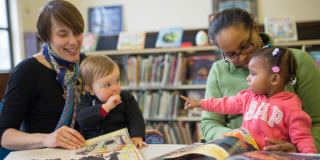 Two library patrons read to toddlers sitting on their laps.