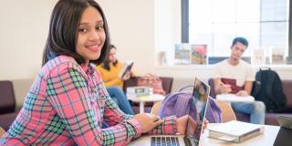 A library patron sits at a desk with a laptop and smiles at the camera
