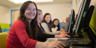 Photograph of a patron smiling at the camera while sitting at a row of desktop computers