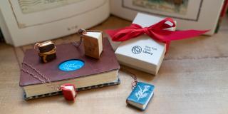 Photograph of several small book pendants arranged near a small gift box tied with a red ribbon that reads: New York Public Library