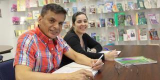 Photo of two patrons sitting side-by-side at a table, holding pens
