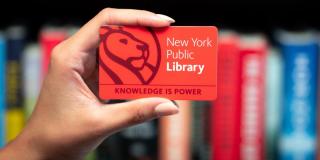 Hand holding a red NYPL library card that reads: New York Public Library, Knowledge Is Power