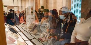 A group of people stand around a display case of historic books, looking at the artifacts within.